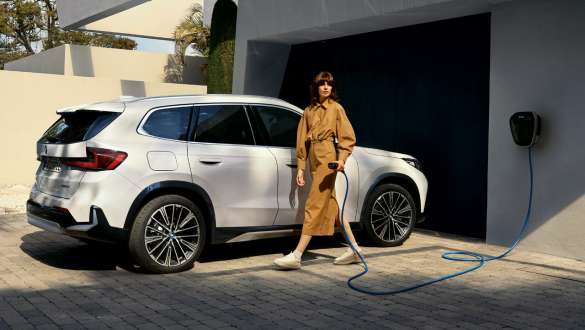 BMW iX1 U11 BEV 2022 davanti al garage Vista laterale a tre quarti della BMW iX1 U11 BEV 2022 Mineral White metallizzato davanti al garage