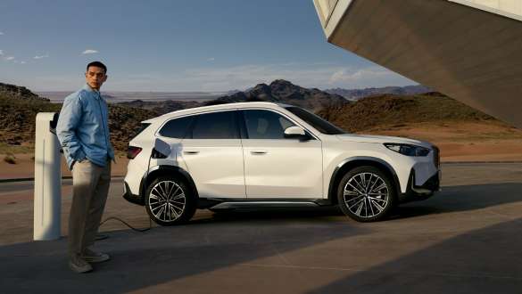 BMW iX1 U11 BEV 2022 in ricarica Vista laterale a tre quarti della BMW iX1 U11 BEV 2022 Mineral White metallizzato davanti al garage