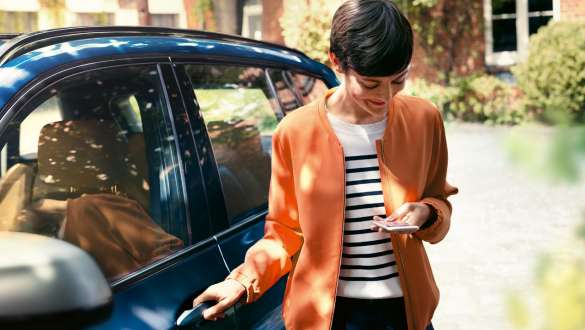 Una donna osserva il proprio smartphone e apre la portiera della sua BMW BMW Teleservice Una donna osserva il proprio smartphone e apre la portiera della sua BMW