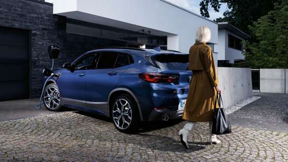 BMW X2 xDrive25e F39 ibrida Plug-in, vista posteriore a quarti a tre quarti in ricarica BMW X2 xDrive25e F39 ibrida Plug-in Vista laterale in ricarica con fotomodella