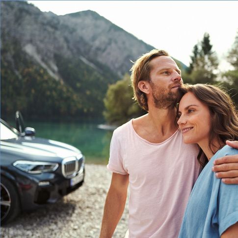 Uomo e donna davanti a una BMW in una vista parziale in estate Controllo vacanze BMW Uomo e donna davanti a una BMW in una vista parziale in estate