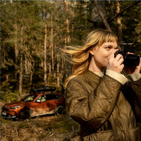 Donna con fotocamera davanti alla BMW in autunno Controllo vacanze BMW Donna con fotocamera davanti alla BMW in autunno