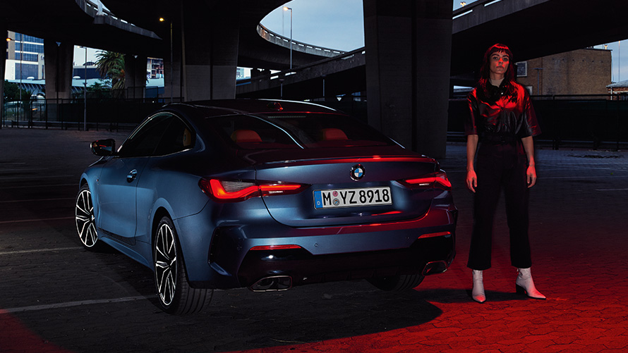BMW Serie 4 Coupé (G22), Arctic Race Blue metallizzato, vista posteriore con persona BMW Serie 4 Coupé (G22), Arctic Race Blue metallizzato, vista posteriore con persona