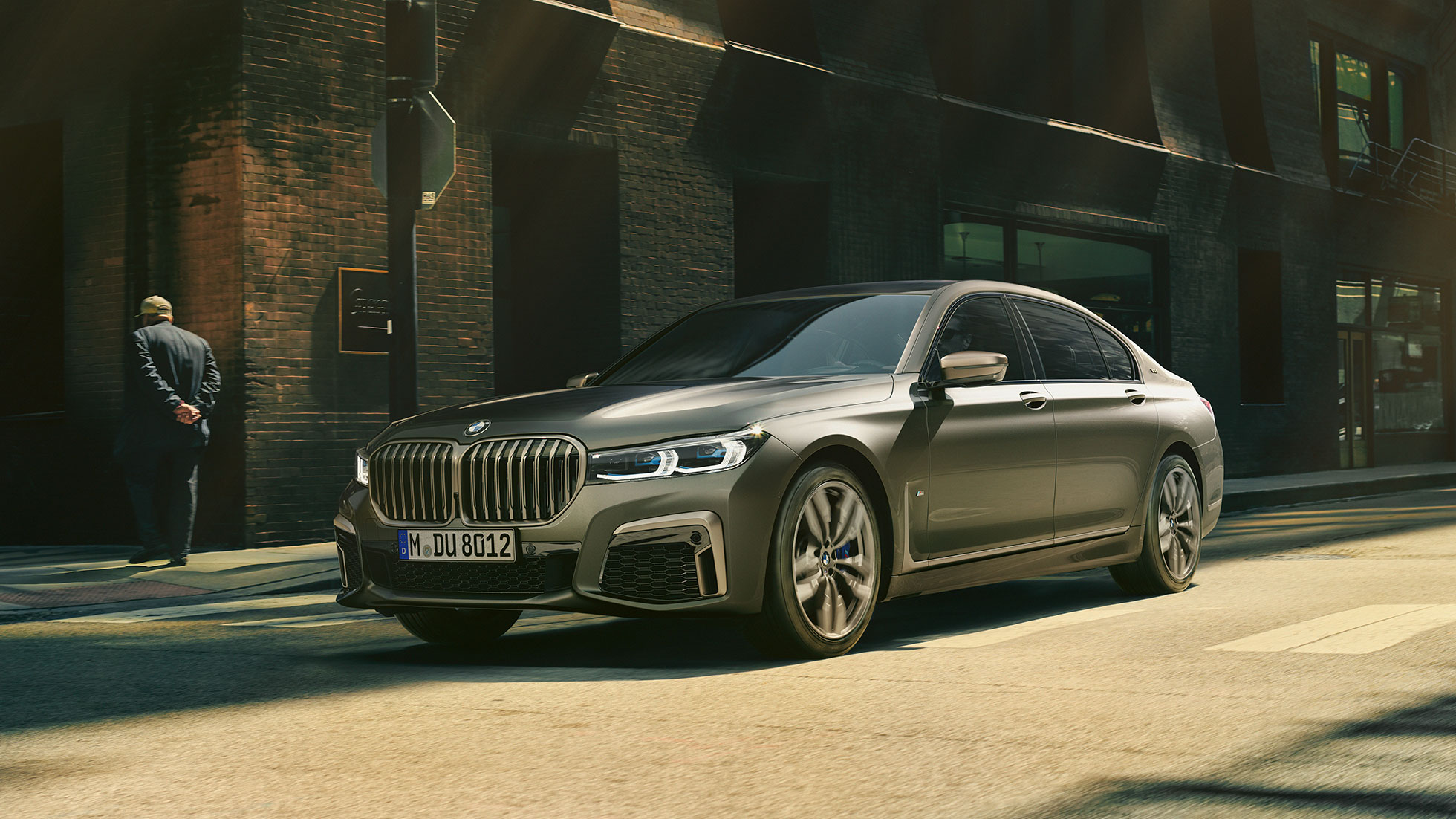 BMW M760Li xDrive dans un décor urbain BMW M760Li xDrive en vue latérale avant, se déplaçant sur une route dans un décor urbain.