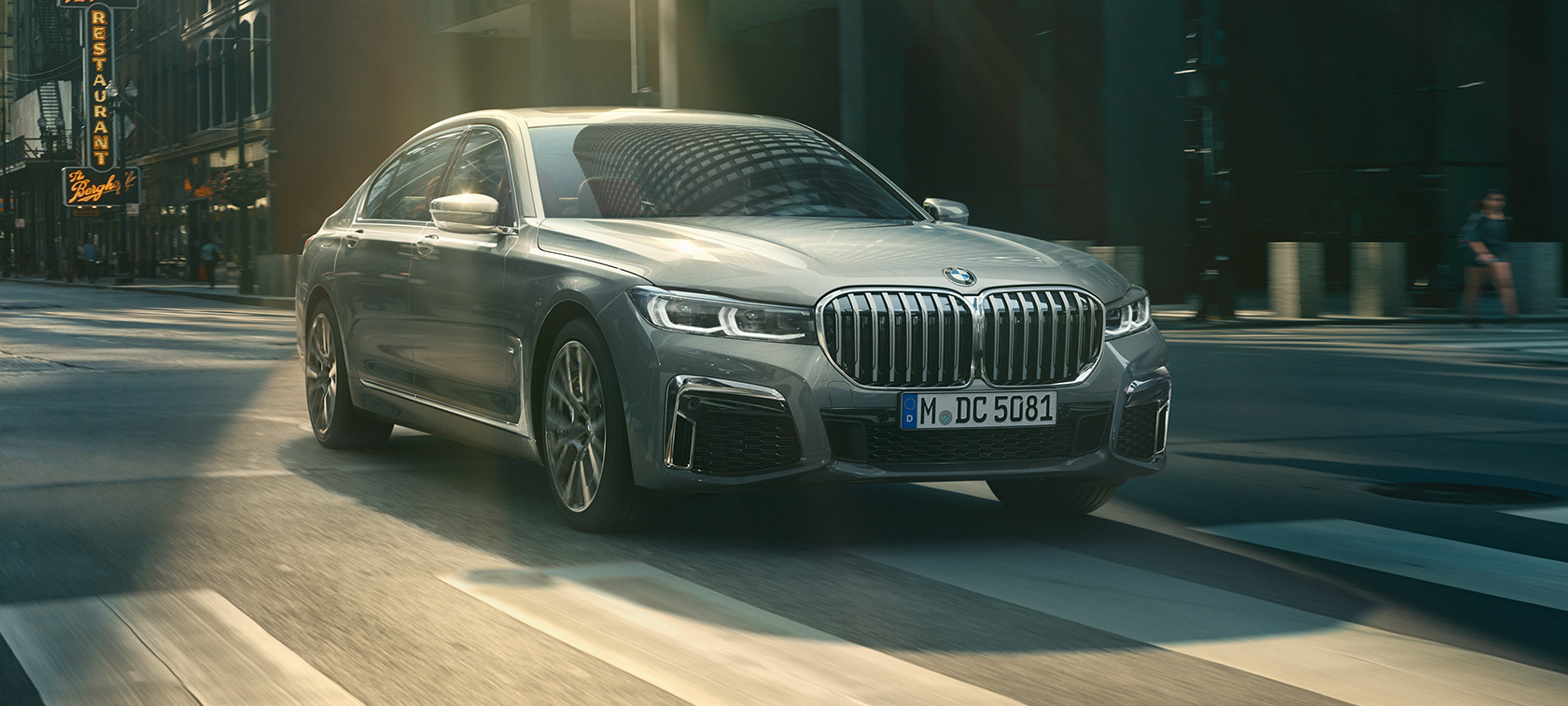 Graue BMW 7er Limousine fahrend, Dreiviertelfrontansicht Graue BMW 7er Limousine fährt in der Dreiviertelfrontansicht durch urbane Kulisse