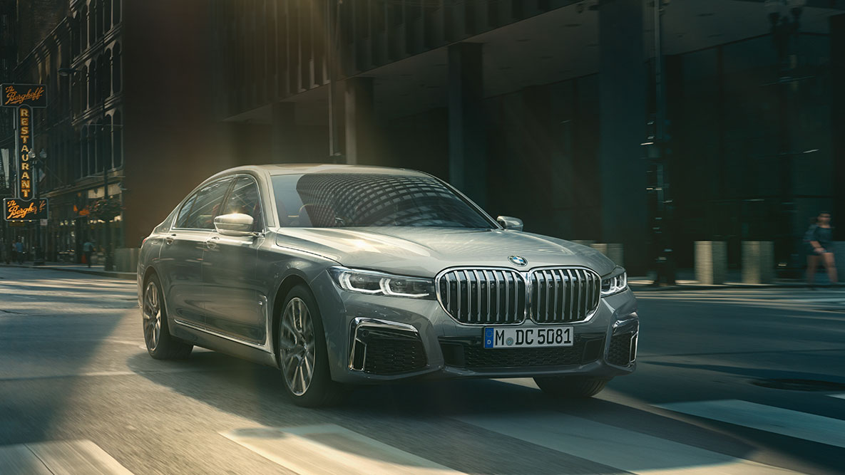 Driving Assistant Professional: Dreiviertelfrontaufnahme der BMW 7er Limousine fahrend vor urbaner Kulisse BMW 7er Limousine Driving Assistant Professional