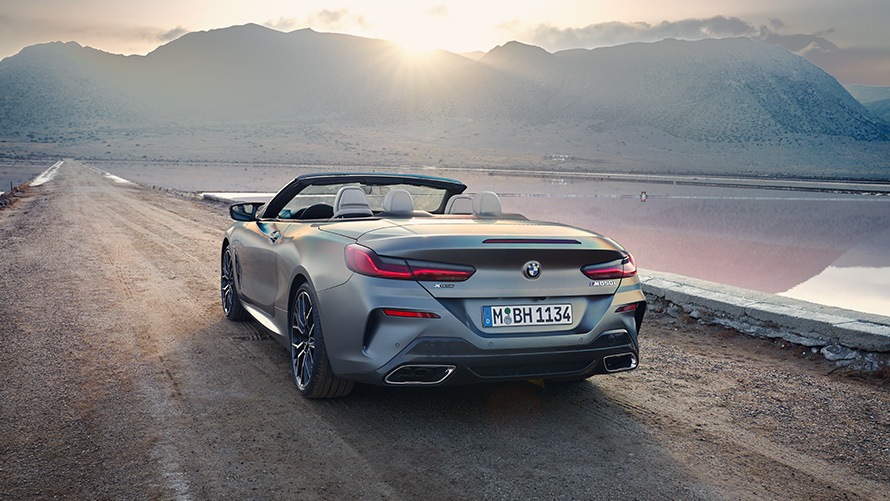 BMW Série 8 Cabrio G14 LCI restylage 2022 Vue arrière avec capote ouverte devant les collines BMW Série 8 Cabrio G14 LCI restylage 2022 Vue arrière BMW Individual Frozen Pure Grey metallic avec capote ouverte debout sur une route de sable avec des collines à l'arrière-plan