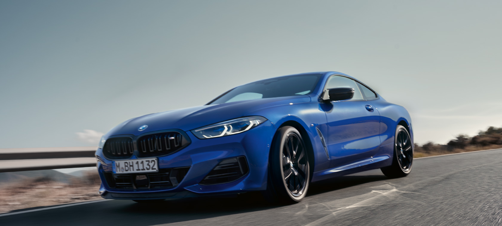 BMW 8er Coupé G15 LCI Facelift 2022 BMW M850i xDrive M Portimao Blau metallic Frontansicht in der Froschperspektive fahrend BMW 8er Coupé G15 LCI Facelift 2022 BMW M850i xDrive M Portimao Blau metallic Frontansicht in der Froschperspektive fahrend auf Landstraße vor hügeliger Landschaft