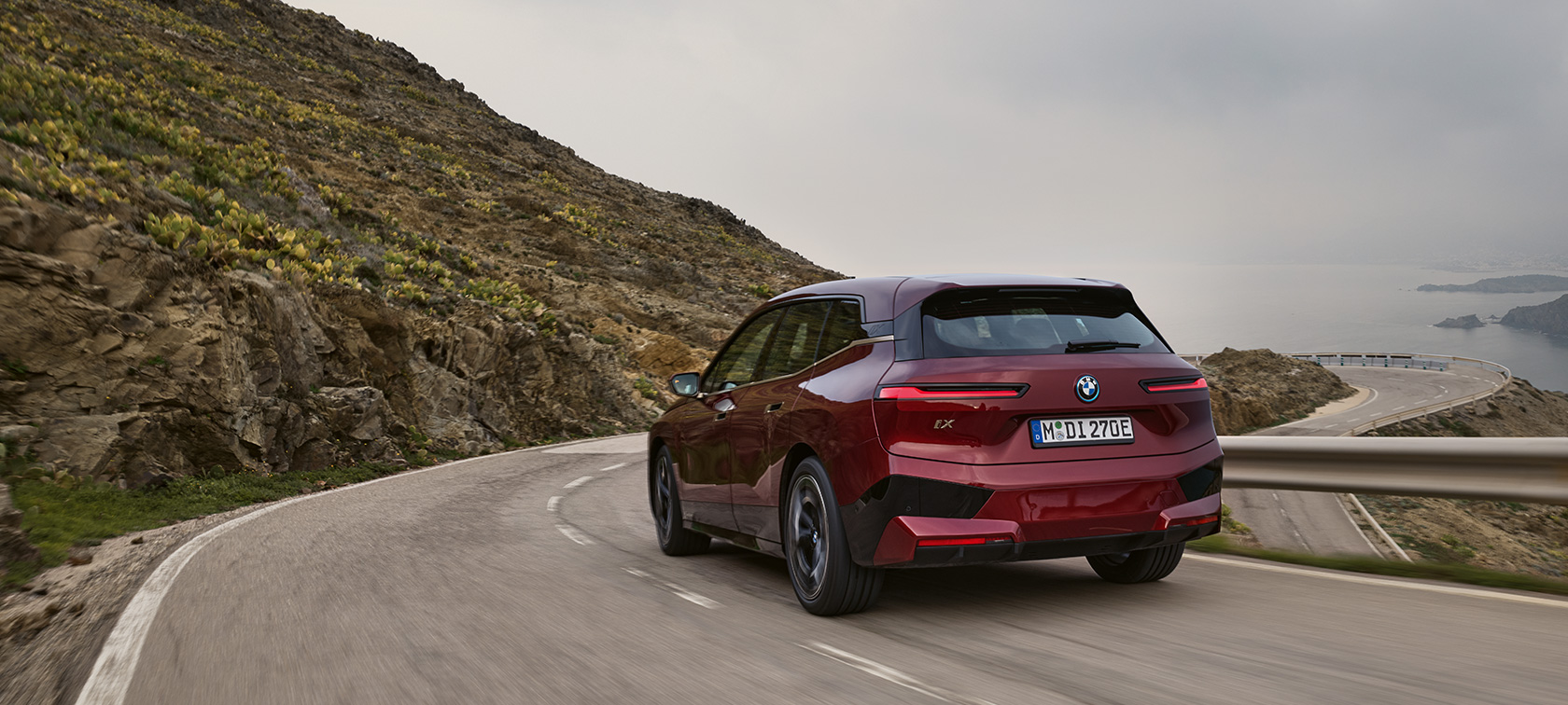 BMW iX i20 2021 SUV elettrico BMW iX xDrive50 in movimento su lungomare BMW iX i20 2021 SUV elettrico BMW iX xDrive50 Aventurine Red Vista posteriore in movimento su lungomare