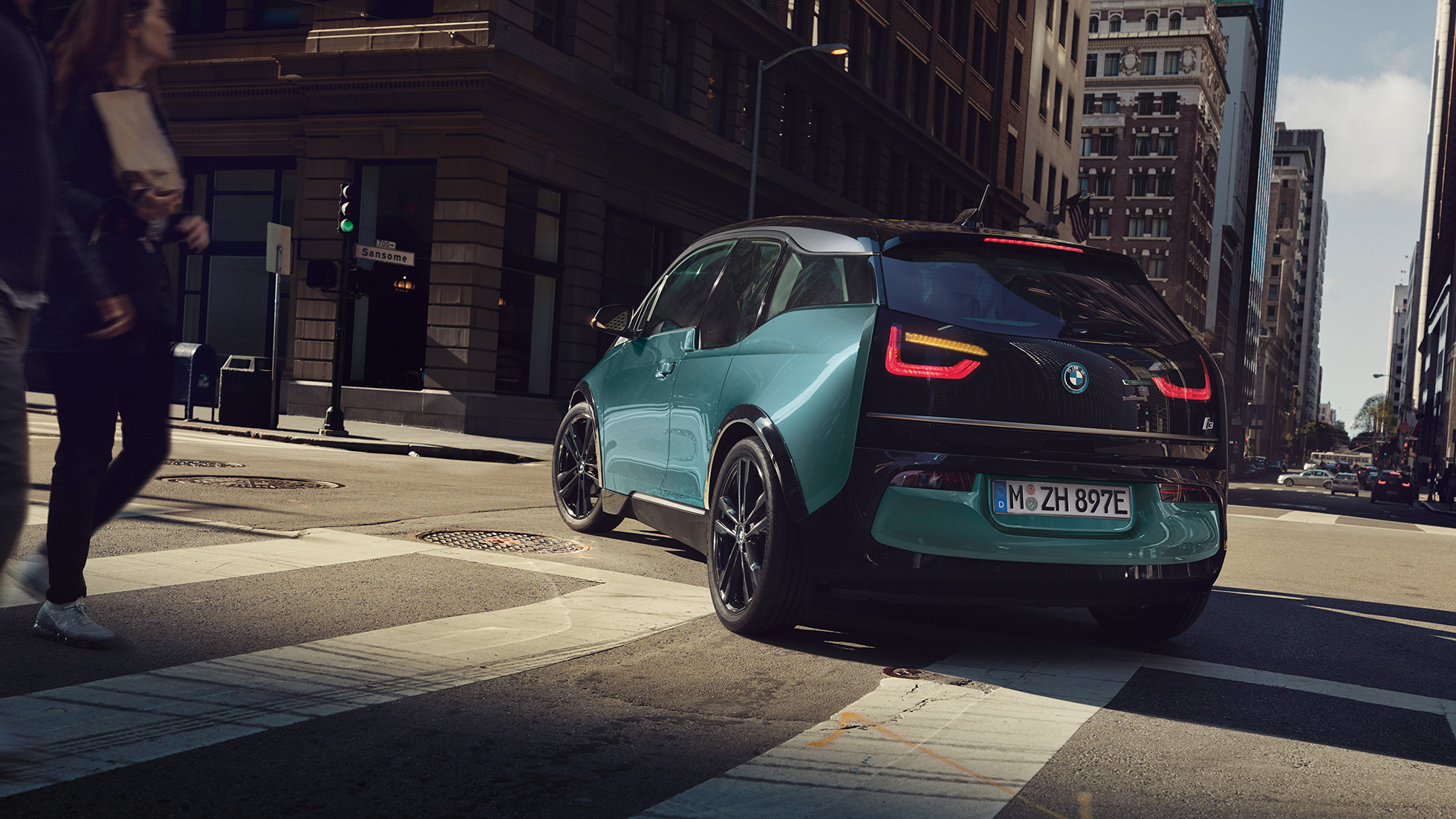 BMW i3 2018 vista posteriore a tre quarti in viaggio I01 BMW i3 I01 2018 Jucaro Beige con profilo in Frozen Grey metallizzato vista posteriore a tre quarti in viaggio su sfondo urbano I01