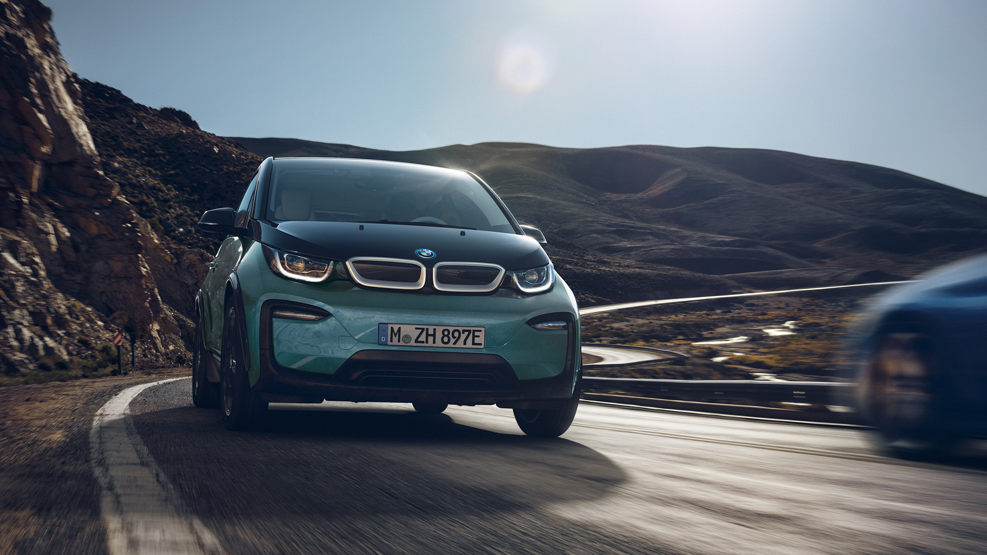 BMW i3 2018 vista laterale in viaggio I01 BMW i3 I01 2018 Jucaro Beige con profilo in Frozen Grey metallizzato vista laterale in viaggio su sfondo urbano I01