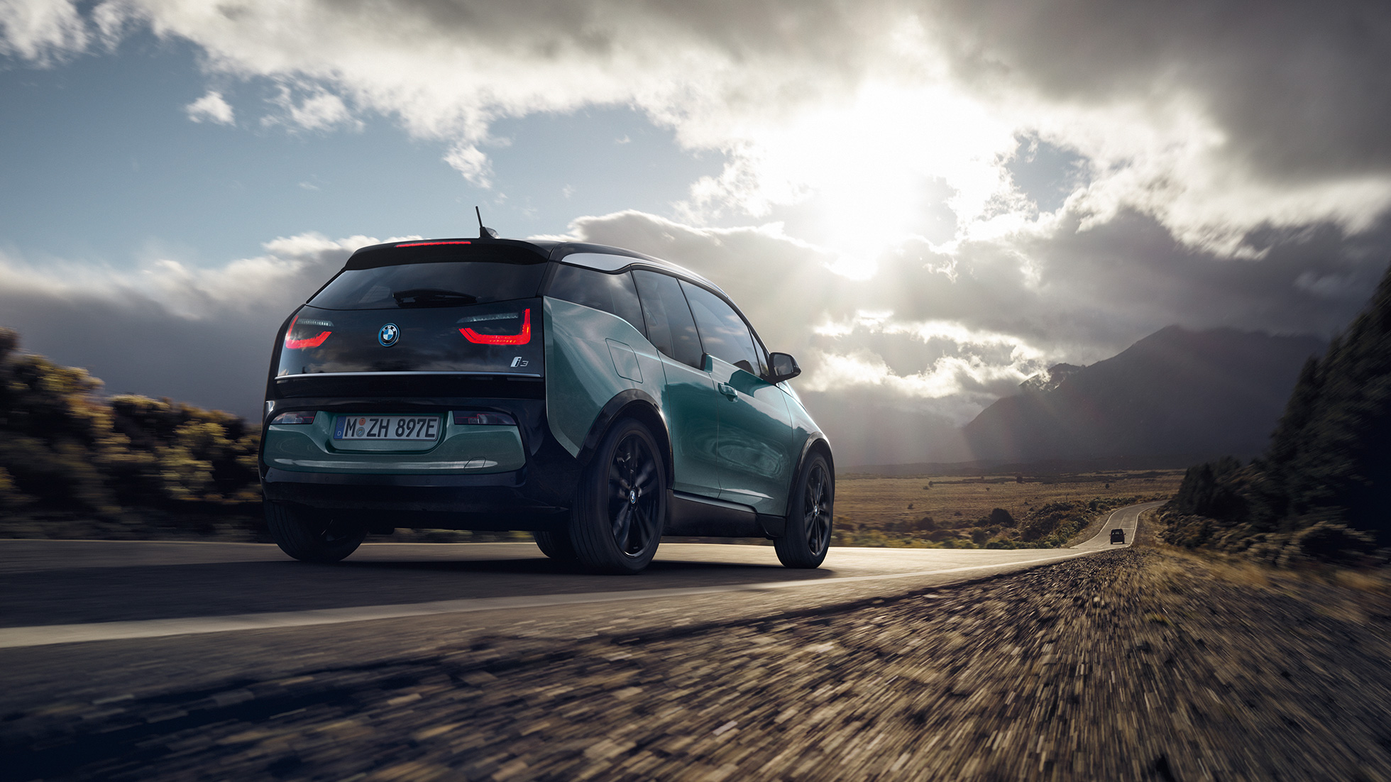 BMW i3 2018 Jucaro Beige vista posteriore a tre quarti in viaggio su una strada provinciale I01 BMW i3 I01 2018 Jucaro Beige con profilo in Frozen Grey metallizzato vista posteriore a tre quarti in viaggio su una strada provinciale I01