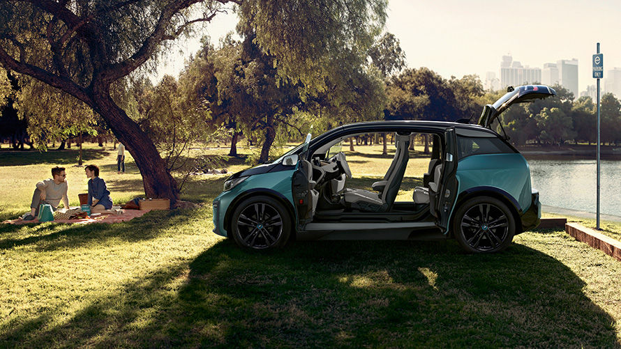 BMW i3 2018 in un parco I01 BMW i3 I01 2018 Jucaro Beige con profilo in Frozen Grey metallizzato vista laterale con porte aperte in un parco I01