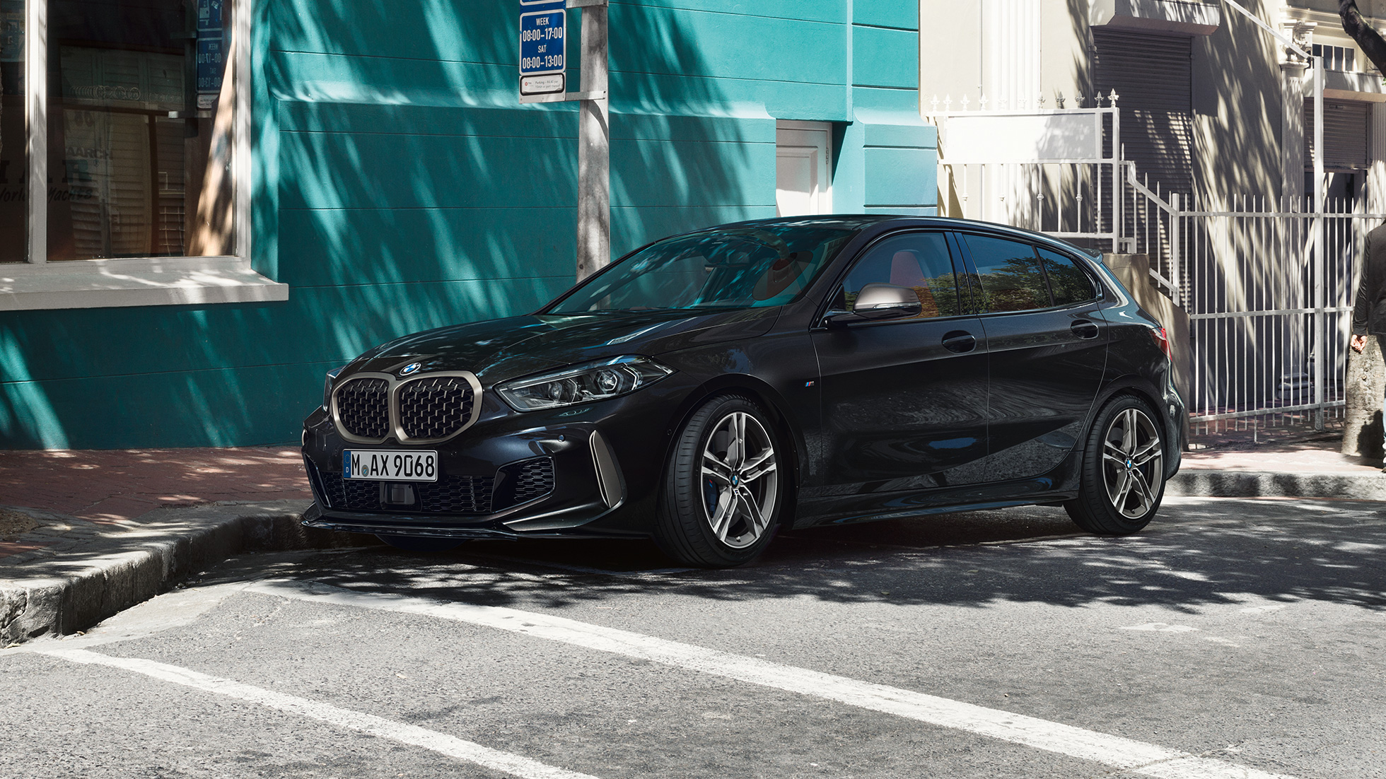 BMW M135i xDrive, vista laterale a tre quarti. F40 BMW M135i xDrive in Sapphire Black metallizzato, vista laterale a tre quarti, mentre sta parcheggiando. F40