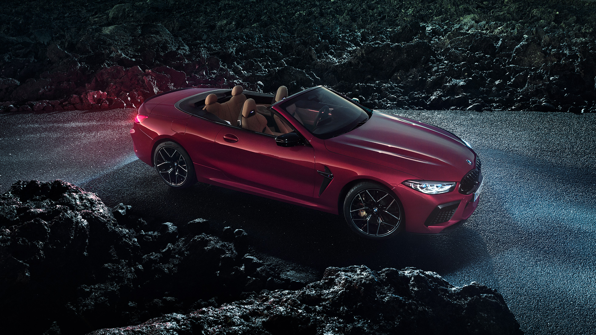 BMW M8 M Competition, vista laterale di tre quarti. F91 BMW M8 Competition Cabriolet in Motegi Red metallizzato con capote aperta, vista laterale di tre quarti, in sosta di notte sull'asfalto. F91