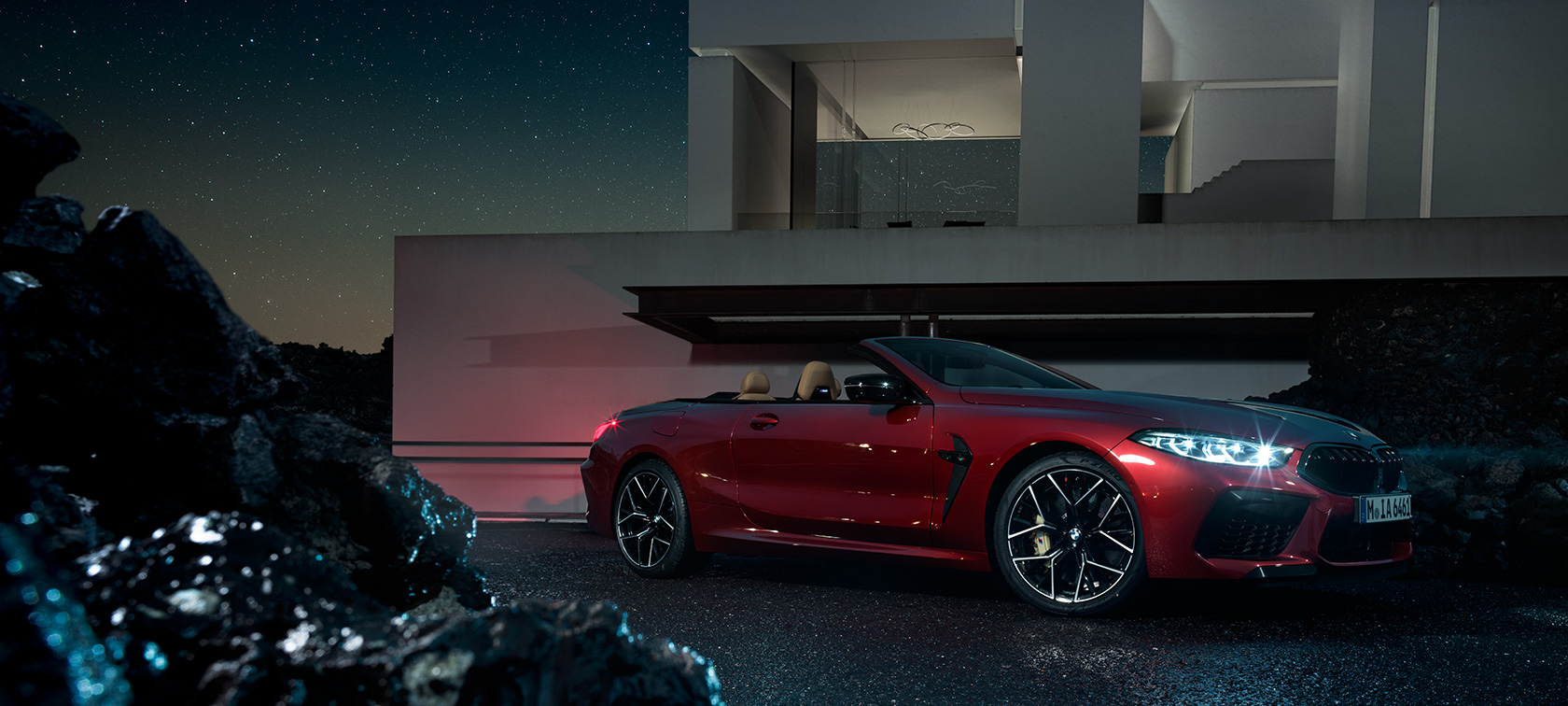 BMW M8 Competition Cabriolet, Dreiviertel-Seitenansicht F91. BMW M8 Competition Cabriolet in Motegi Rot metallic, Dreiviertel-Seitenansicht, stehend bei Nacht vor Villa F91.