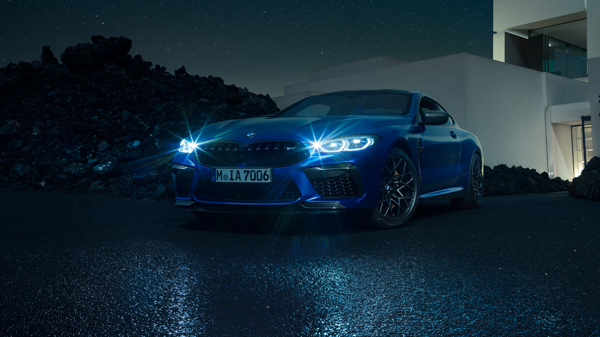 BMW M8 M Competition Coupé, vista frontale di tre quarti. F92 BMW M8 Competition Coupé in Marina Bay Blue metallizzato con fari a LED accesi, vista frontale di tre quarti in sosta davanti a una villa di notte. F92