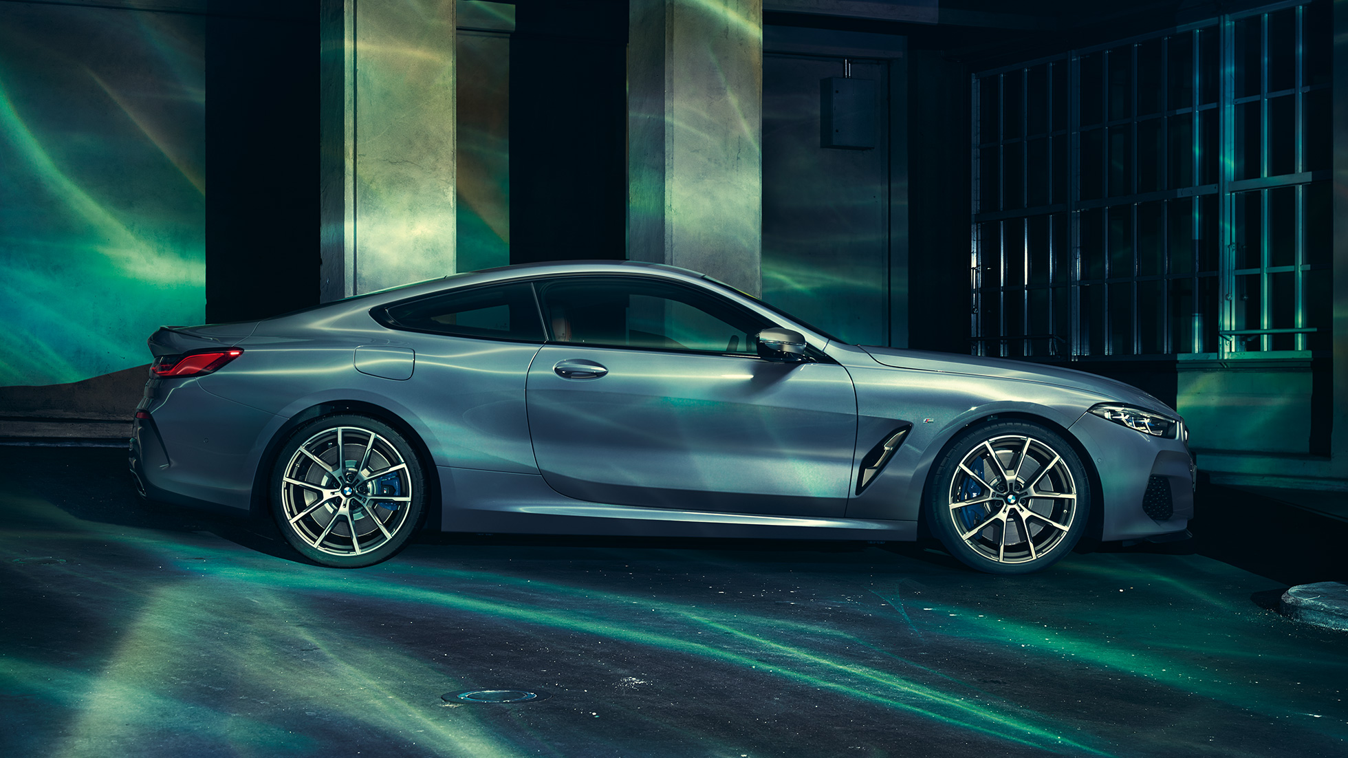 BMW M850i xDrive Coupé, vista laterale. G15 BMW M850i xDrive Coupé in Barcelona Blue metallizzato, vista laterale, in sosta davanti a un edificio. G15