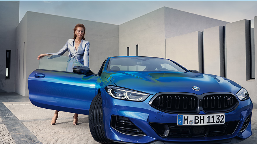 BMW M850i xDrive Coupé G15 LCI Facelift 2022 M Portimao Blue metallizzato vista anteriore da ferma con modella a portiera lato passeggero aperta