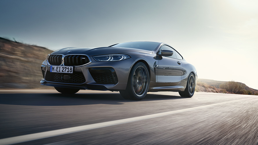BMW M8 Coupé F92 LCI Facelift 2022 Skyscraper Grey metallizzato vista anteriore a tre quarti in movimento su strada provinciale con prospettiva dal basso