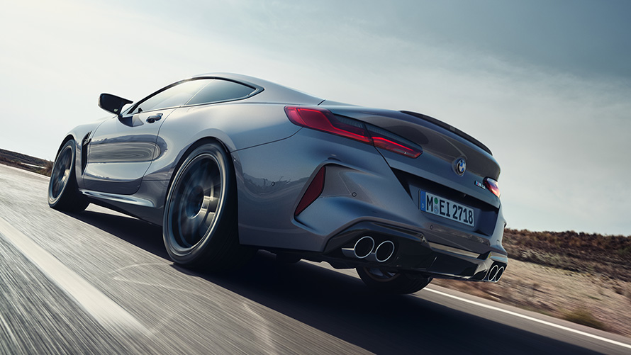 BMW M8 Coupé F92 LCI Facelift 2022 Skyscraper Grey metallizzato, vista posteriore a tre quarti in movimento su strada provinciale con prospettiva dal basso
