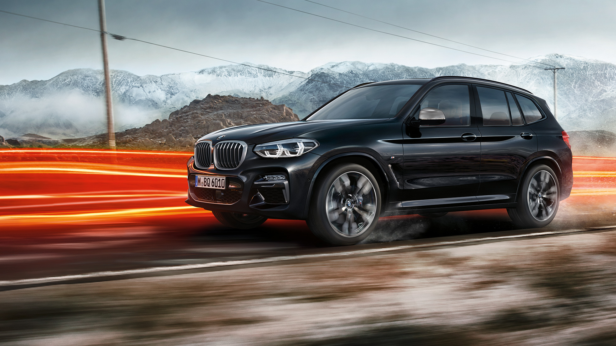 BMW X3 M40i e BMW X3 M40d, vista laterale. BMW X3 M40i e BMW X3 M40d in Sapphire Black metallizzato, in movimento, esterni, vista laterale su sfondo collinare con strisce di luce.