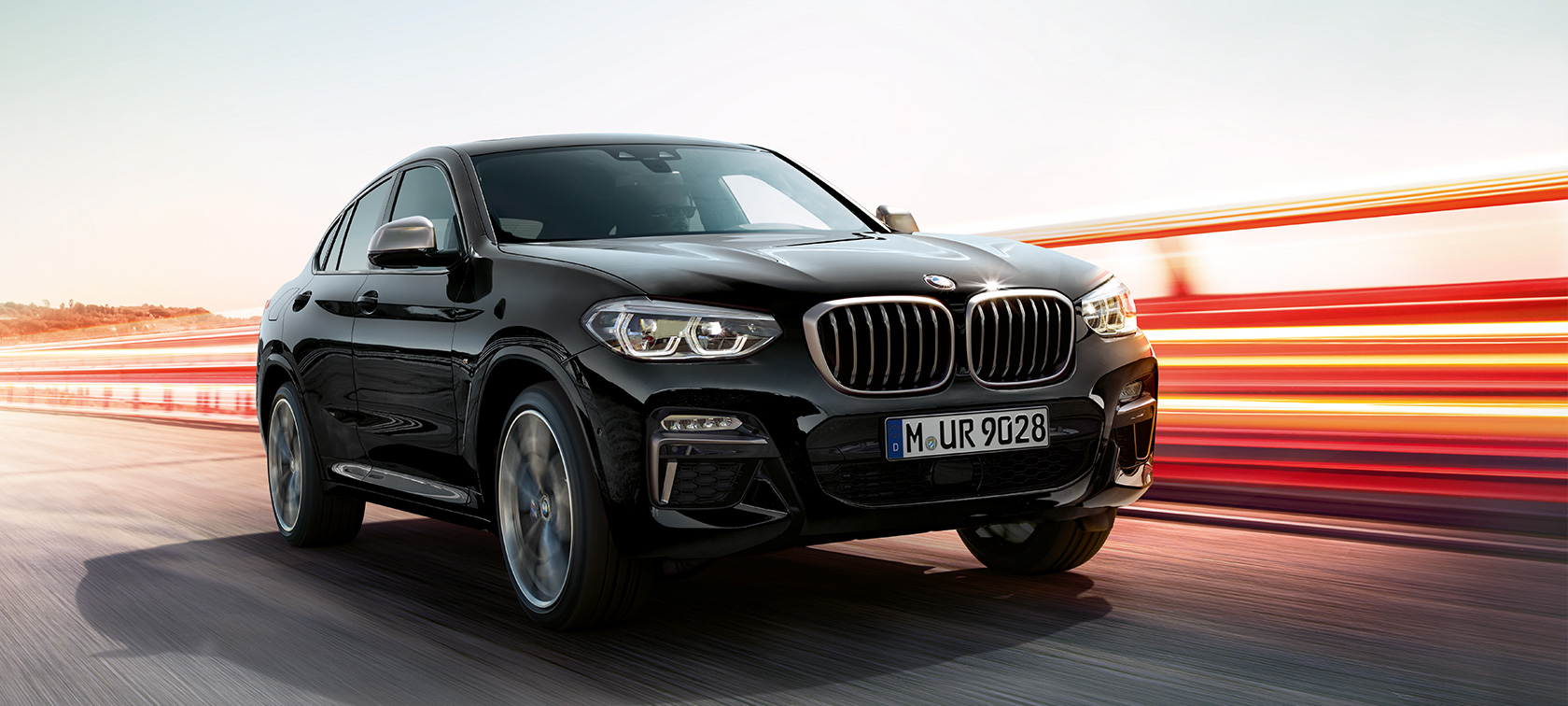 BMW X4 M40i e BMW X4 M40d, vista anteriore sinistra a tre quarti. G02 BMW X4 M40i e BMW X4 M40d in Sapphire Black metallizzato, in movimento, esterni, vista anteriore a tre quarti sinistra con strisce di luce. G02