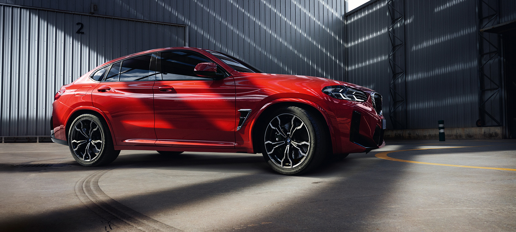 Vista anteriore a tre quarti della BMW X4 M F98 LCI Facelift 2021 BMW X4 M F98 LCI Facelift 2021 Toronto Red metallizzato Vista anteriore a tre quarti in un capannone