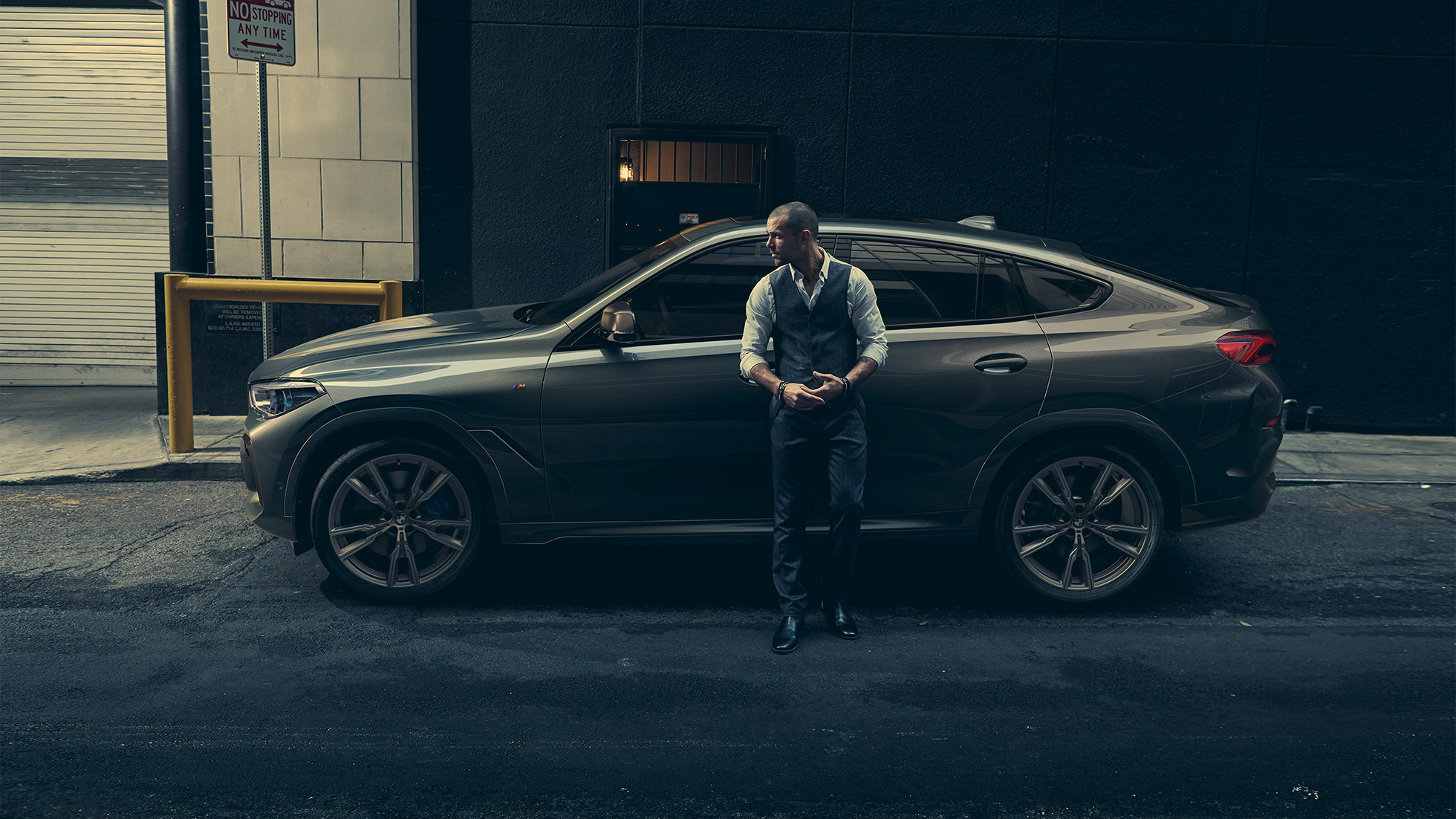 BMW X6 M 50i in vista laterale Vista laterale di un uomo appoggiato alla BMW X6 M50i in ambiente urbano