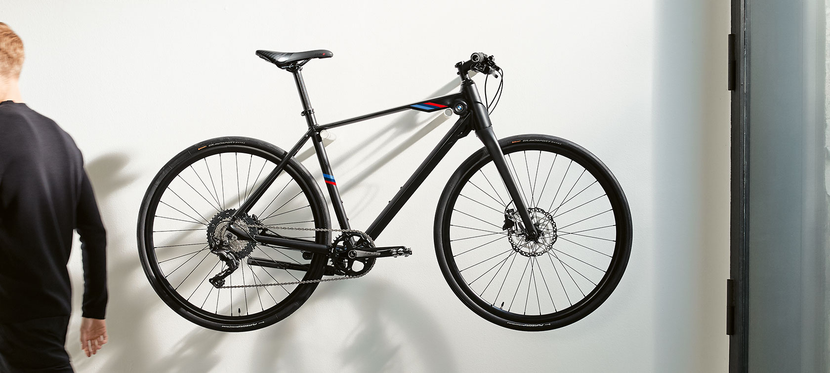 BMW M Bike. Das Bild zeigt das BMW M Bike mit den BMW M Motorsport Streifen an einer Wandhalterung.