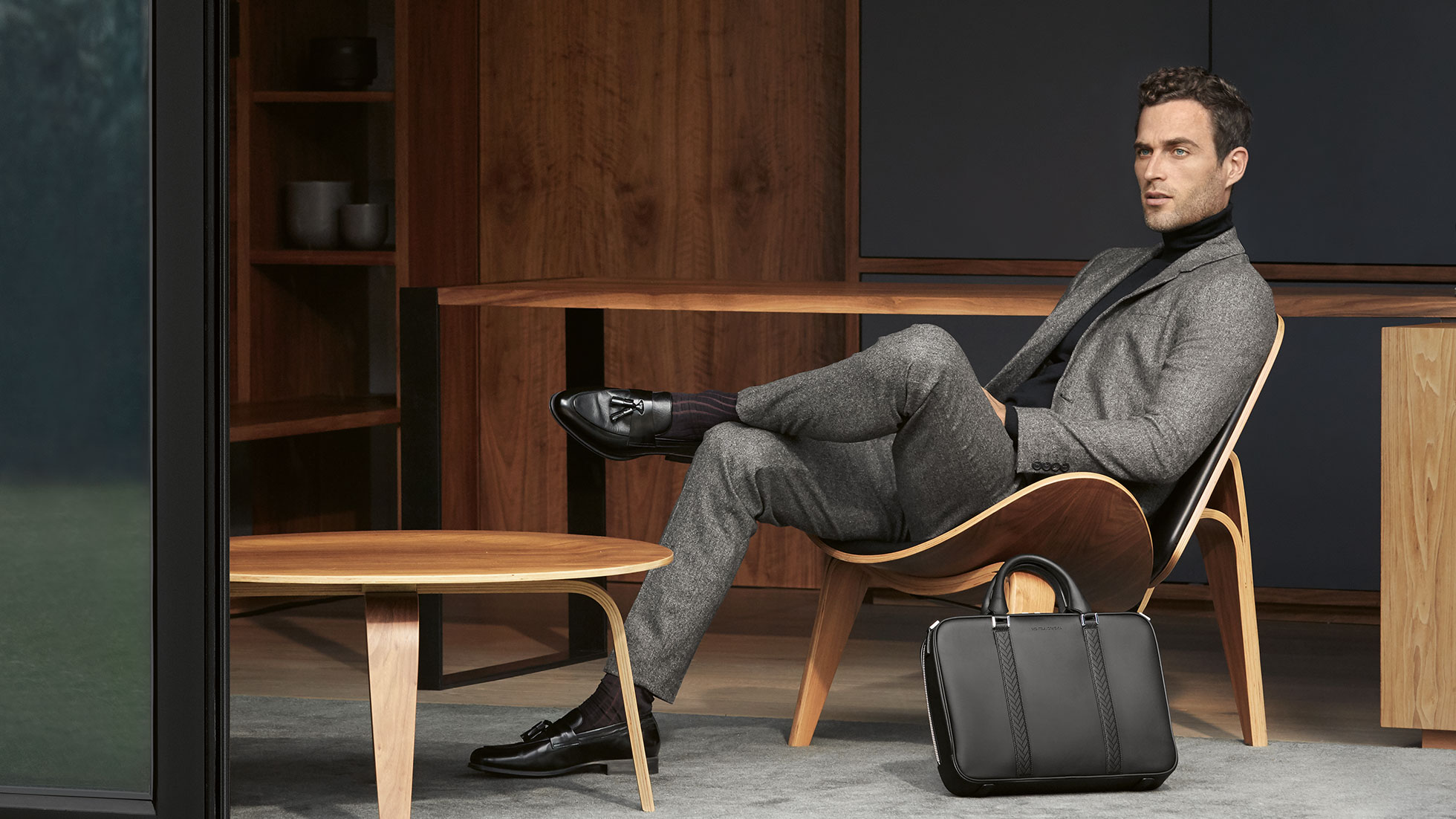 The Collection. Im Bild präsentiert ein sitzender Mann im Anzug Kollektionsteile der The Collection.