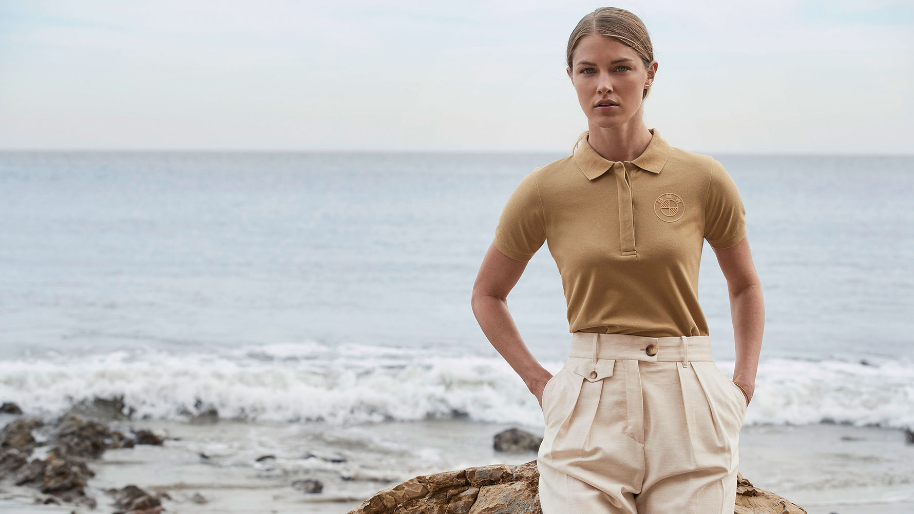 Una ragazza indossa la polo con logo BMW, da donna, di fronte allo sfondo di una spiaggia. Una ragazza indossa la polo con logo BMW, da donna, di fronte allo sfondo di una spiaggia.