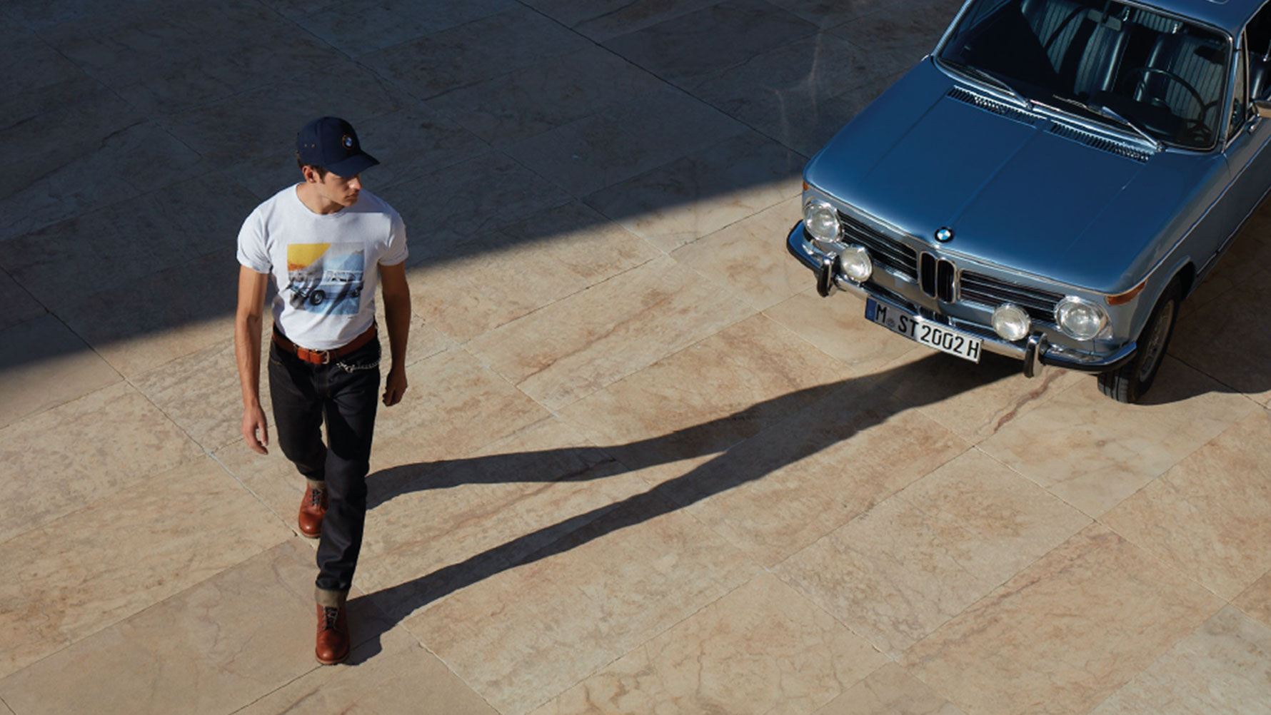 Un uomo indossa la T-shirt BMW Classic, da uomo, della collezione BMW Classic Collection e ammira una BMW d’epoca. Un uomo indossa la T-shirt BMW Classic, da uomo, della collezione BMW Classic Collection e ammira una BMW d’epoca.
