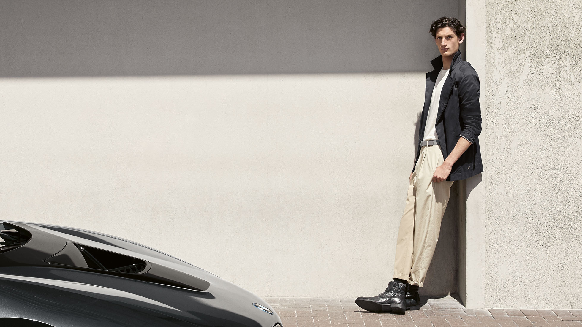 BMW i Collection. La foto mostra un uomo appoggiato a un muro con una giacca BMW i della BMW i Collection.