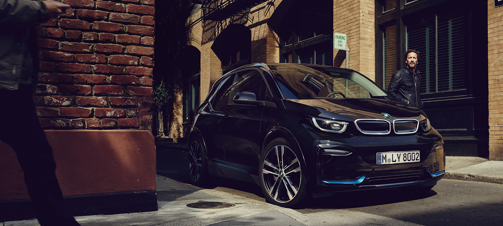 BMW i3. BMW i3 in Dreiviertel-Front vor urbaner Kulisse.