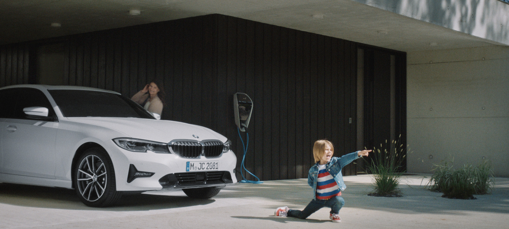BMW Hybridfahrzeug an Ladestation BMW Plug-in-Hybride Junge vor BMW Hybridfahrzeug an Ladestation