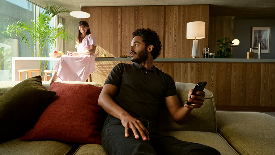 Partage de BMW Digital Key Partage de BMW Digital Key, homme avec un smartphone dans les mains assis sur le canapé avec femme en arrière-plan