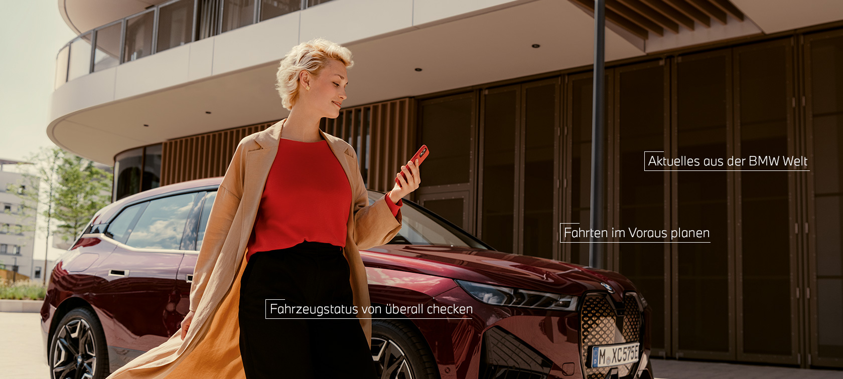 Frau vor BWW iX und benutzt My BMW App auf Smartphone
