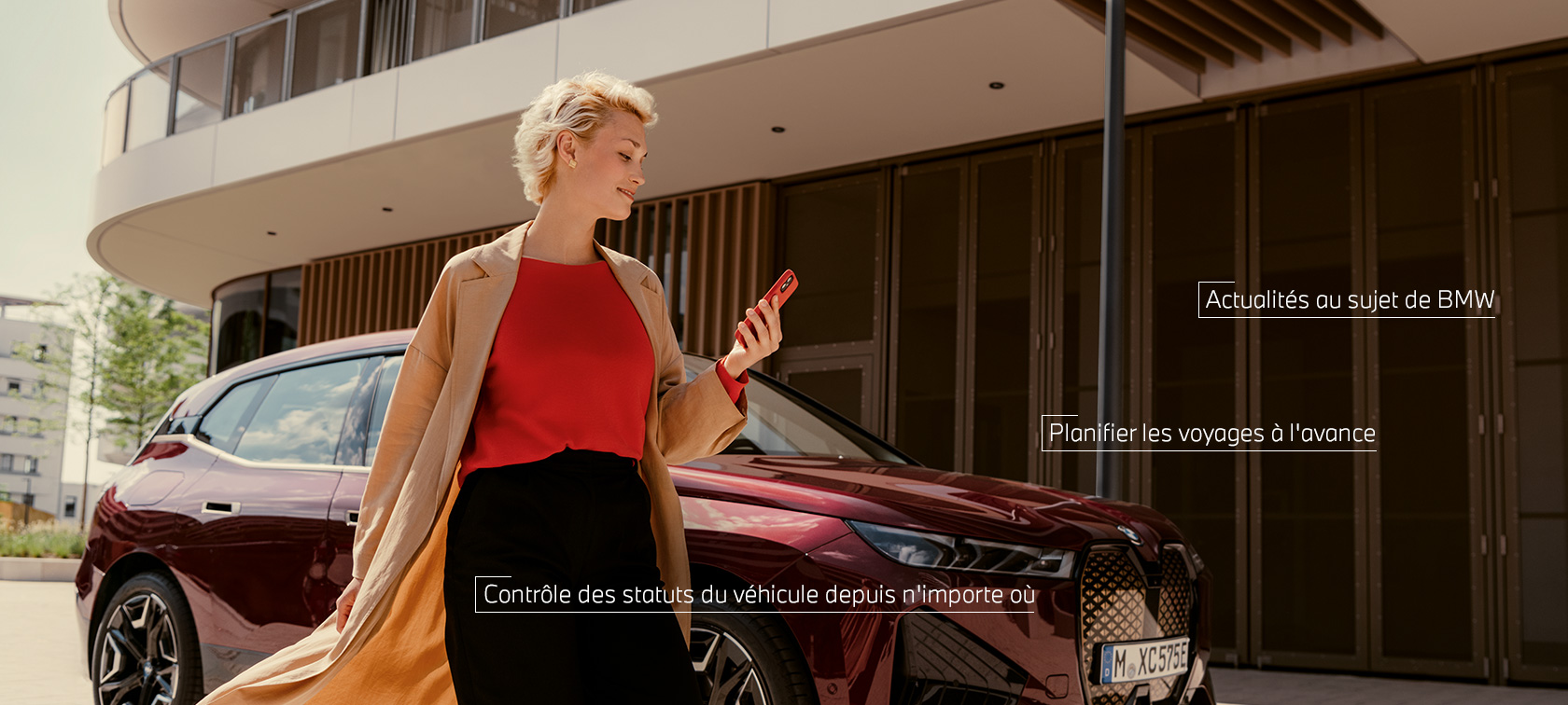 Une femme se tient devant une BMW X5 blanche et utilise l’App My BMW sur smartphone.
