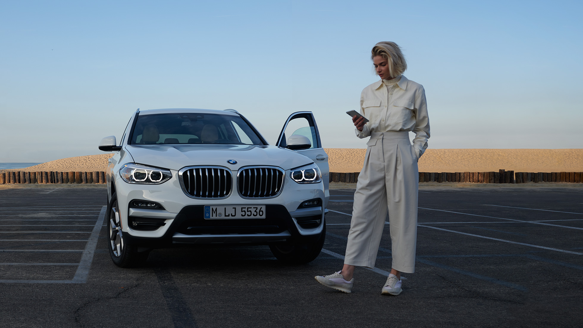 Frau benutzt My BMW App auf dem Smartphone Frau benutzt My BMW App von BMW ConnectedDrive auf dem Smartphone vor weissem BMW X5