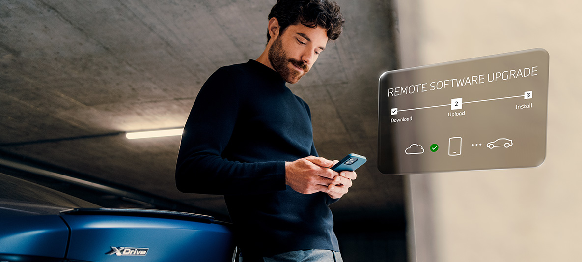 Homme appuyé à l'arrière de la BMW et regardant son smartphone Remote Software Upgrade homme appuyé à l'arrière de la BMW et regardant son smartphone