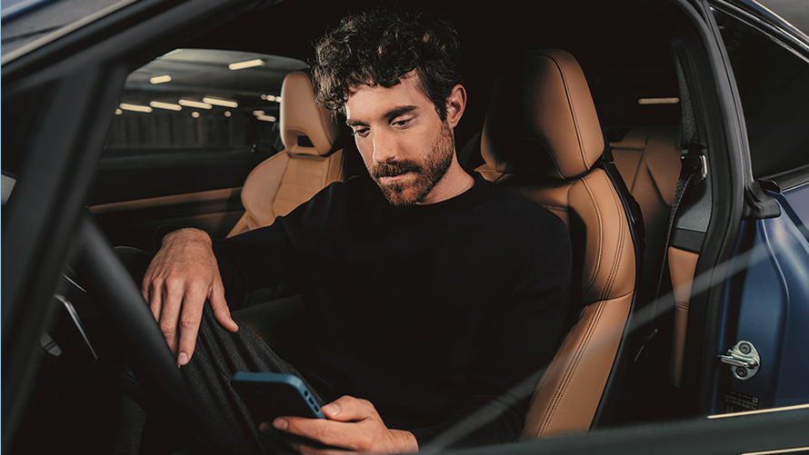 Un uomo è seduto in una BMW Un uomo seduto in una BMW guarda il proprio smartphone