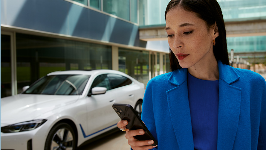 Una donna davanti a una BMW Una donna davanti a una BMW con sguardo sul proprio smartphone