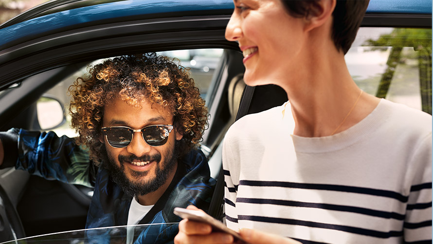 BMW Connected Mann im BMW und Frau ausserhalb des BMW nutzen BMW Connected auf dem Smartphone