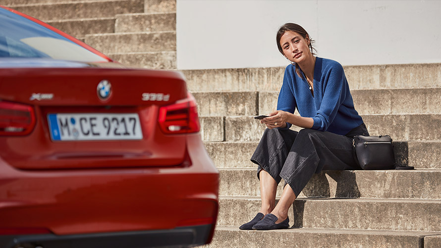 Service & Pannenhilfe Frau sitzt vor ihrem roten BMW und nutzt die Service & Pannenhilfe