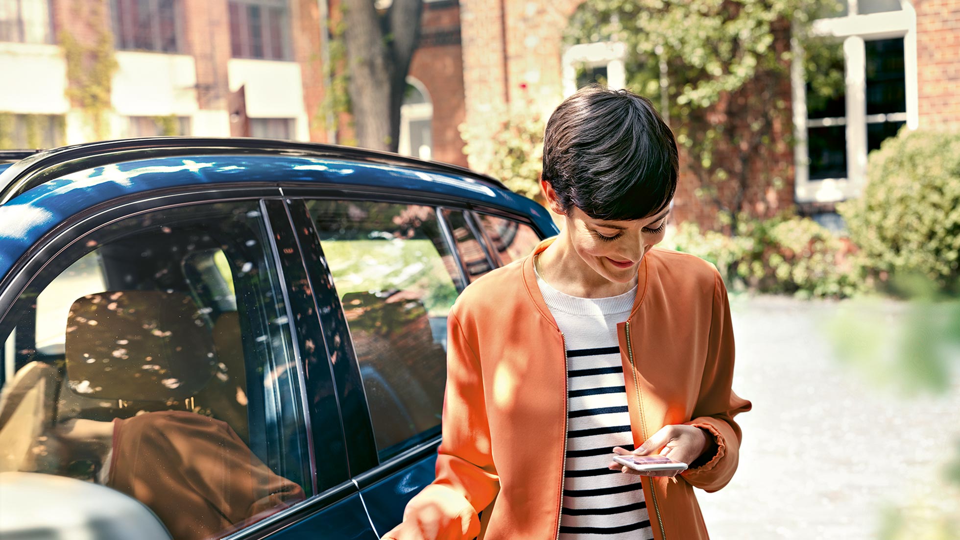 Pacchetto All In BMW, leasing Donna in piedi davanti all’auto, guarda sorridendo il display del cellulare.