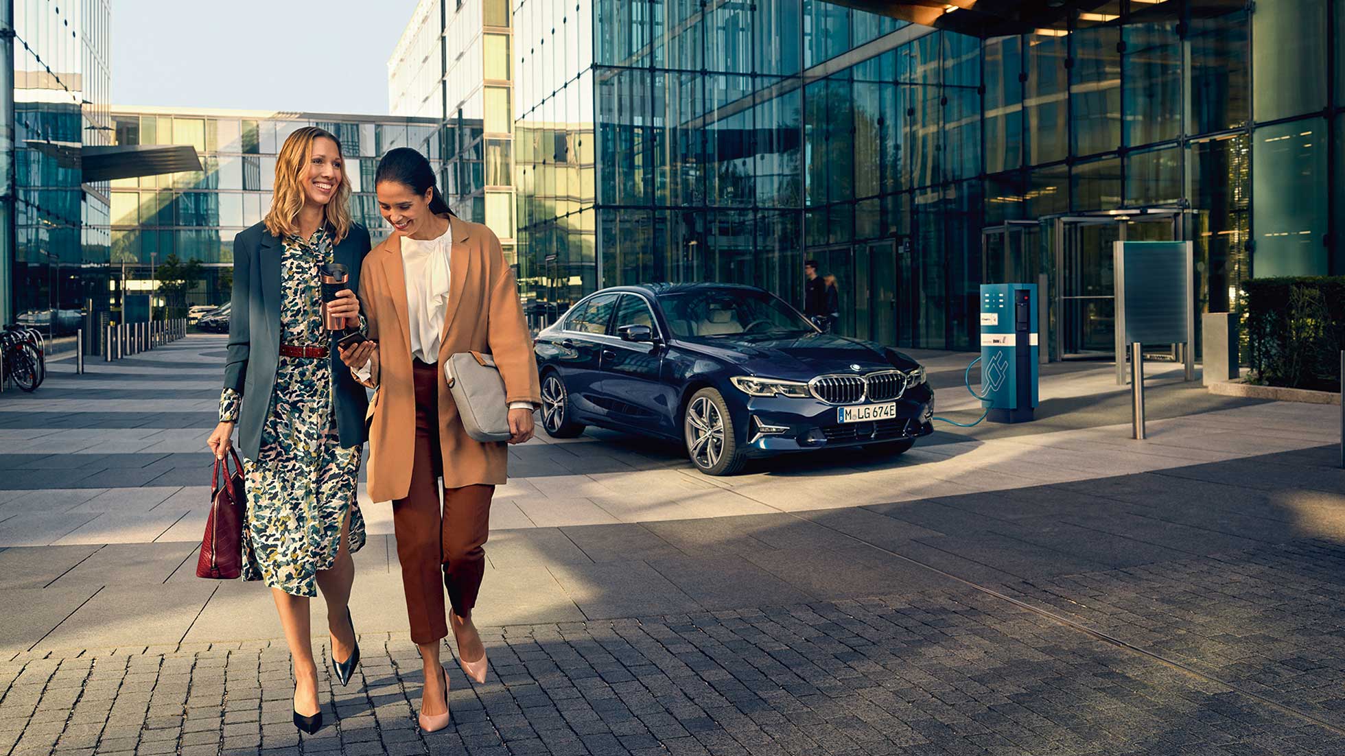 Pacchetto All In BMW, assicurazione Due donne, allacciate, si allontanano dall’auto attraverso una piazza.