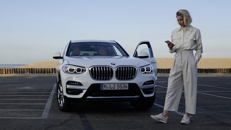 Une femme avec un téléphone portable devant une BMW garée