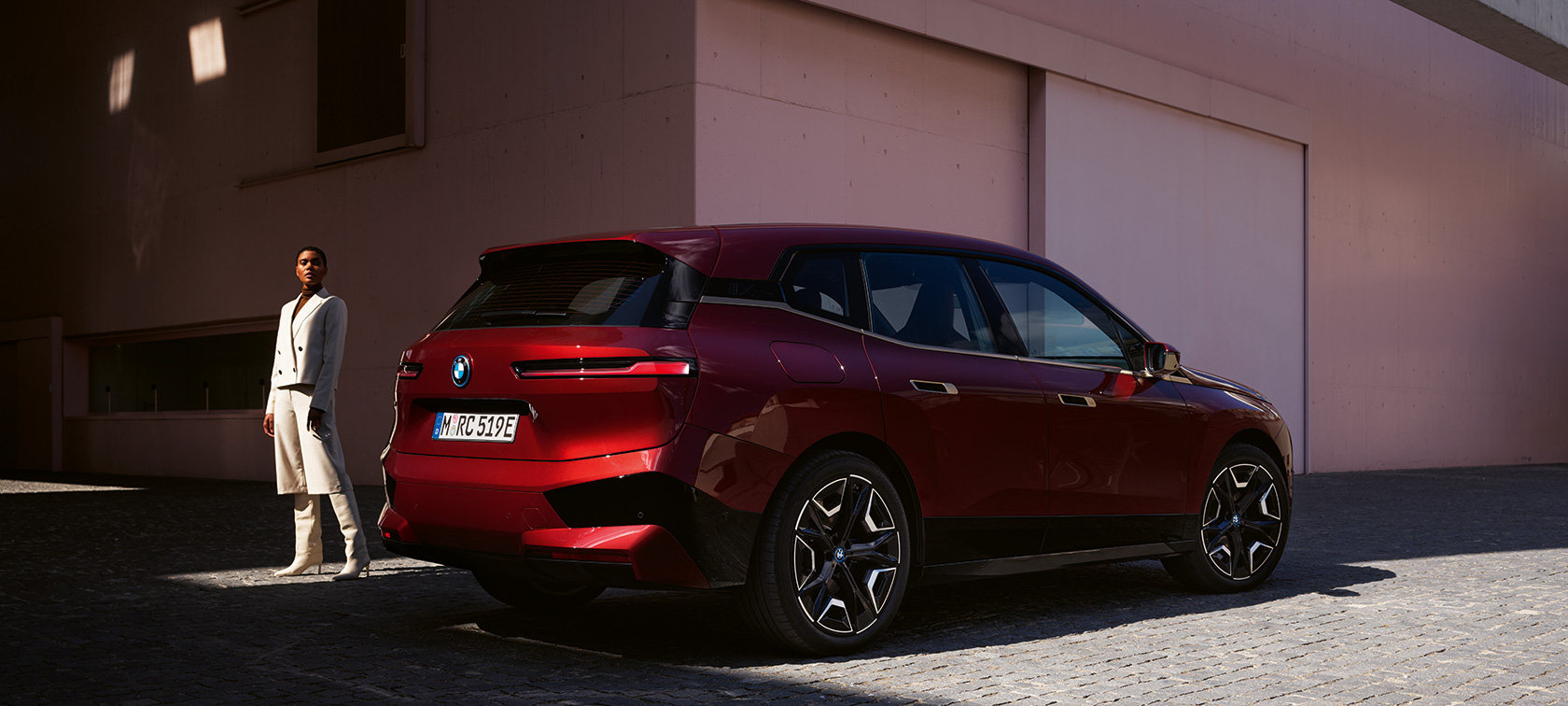 BMW iX Aventurinrot Dreiviertel-Seitenansicht vor Gebäude mit Model BMW iX Aventurinrot Dreiviertel-Seitenansicht vor Gebäude mit Model