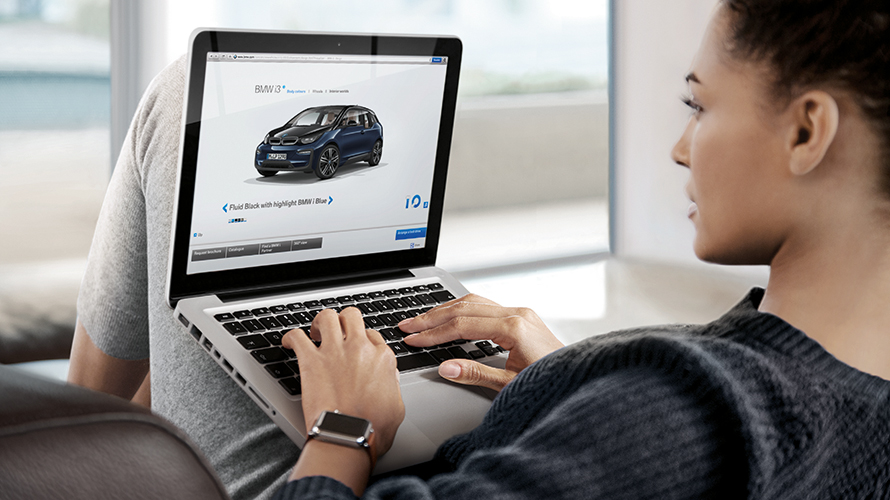 Femme avec ordinateur portable BMW i3 bleu-noir vue de côté canapé salon avec fenêtre 